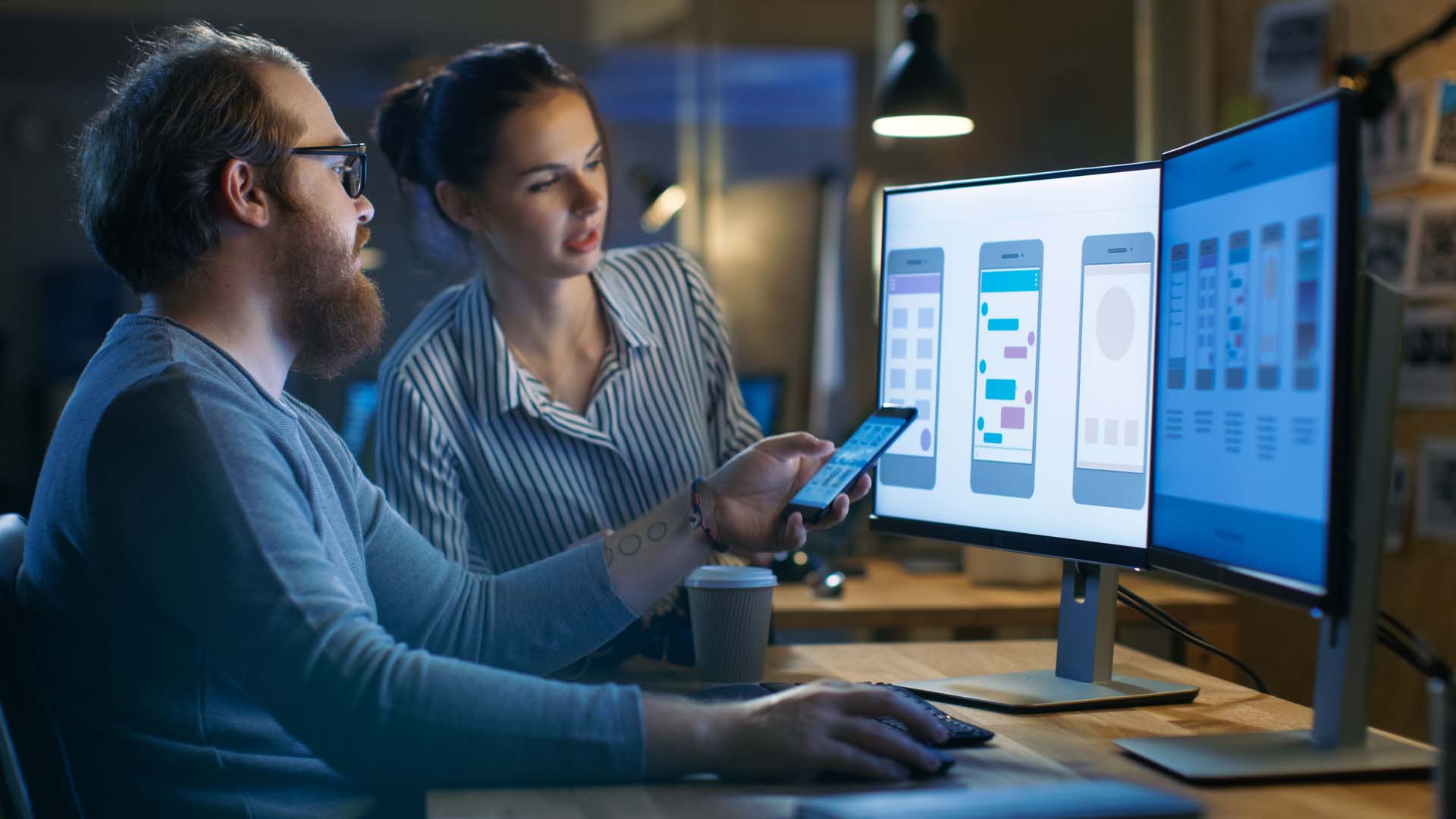 MAle-and-female-looking-at-monitors-mobile-in-hand-iStock-846843314