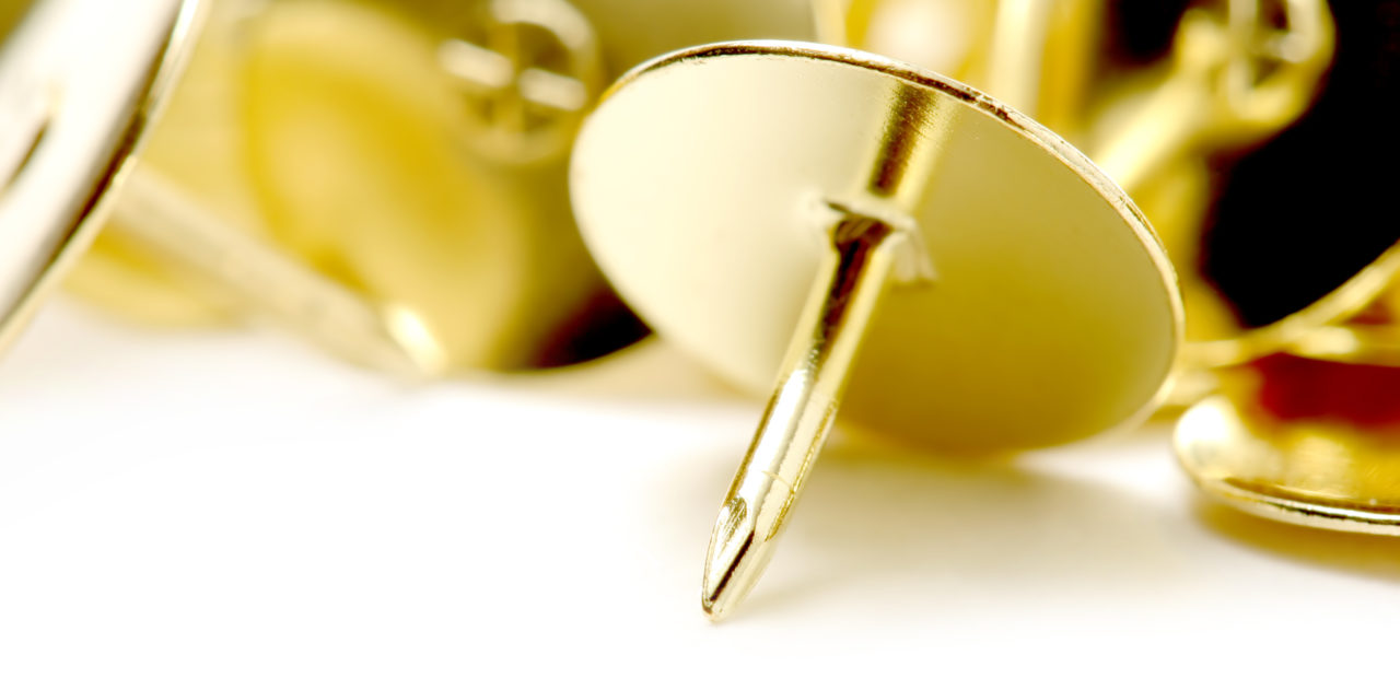 Close-up image of a golden thumbtack on a white background, symbolizing precision and detail in panel design, the fundamentals of panel design