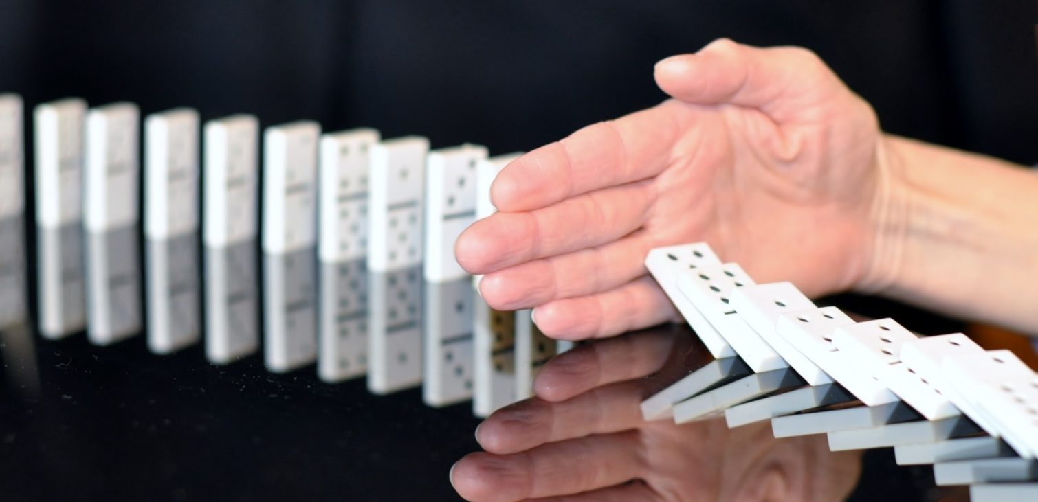 A person's hand intervening to stop a row of falling dominoes, proactive measures in systems simulation lifecycle management.