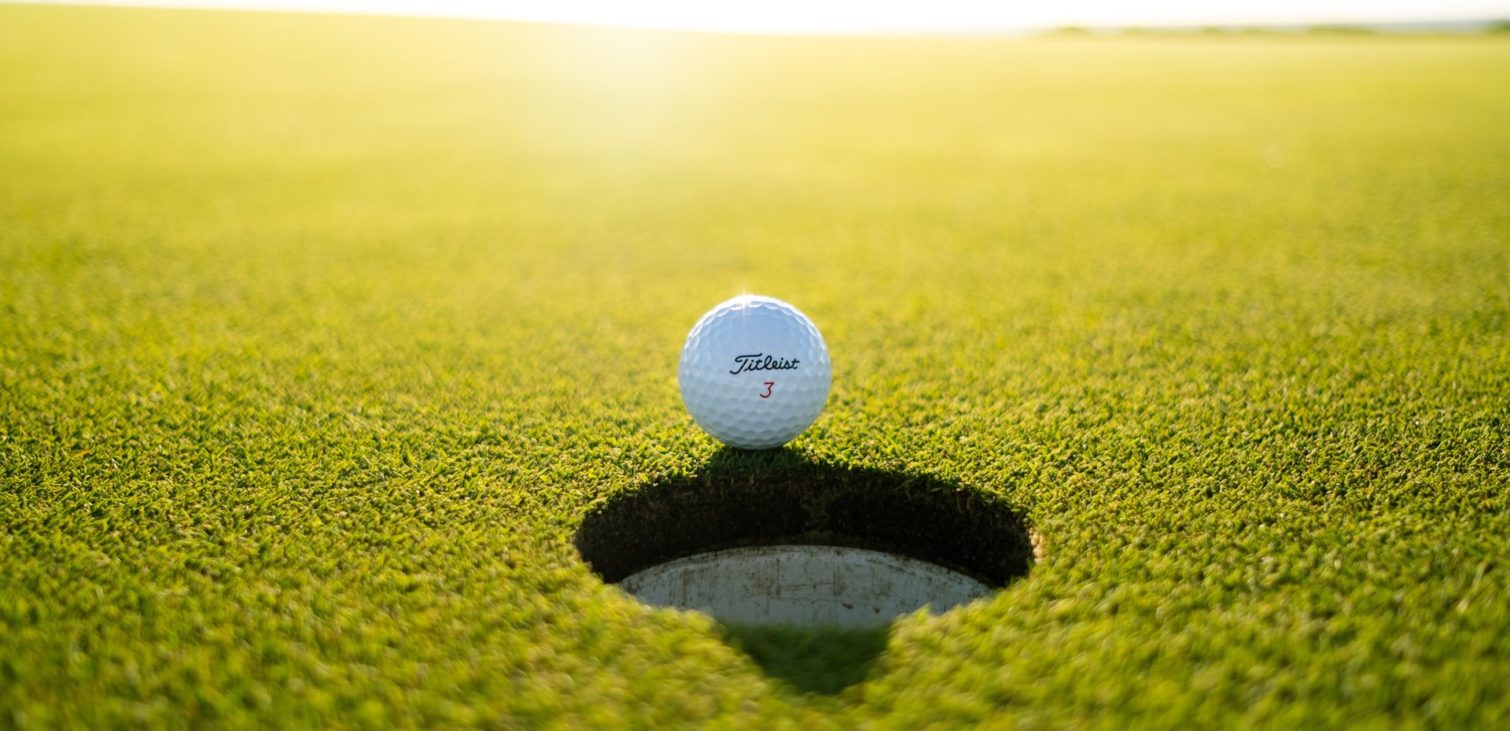 A golf ball teetering on the edge of a hole on a lush green golf course, an envision of the Zuken golf day out as the suspense of nearly putting the golf ball