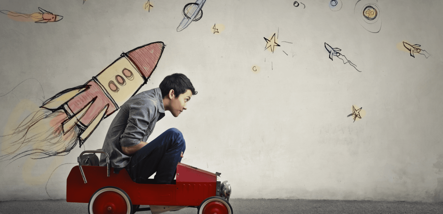 Boy in a small red car with a rocketship drawn behind him