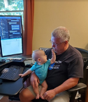 Zuken staff member sitting at his desk with a young baby in his lap