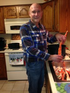 A man in a kitchen holding a king crab leg at the sink.