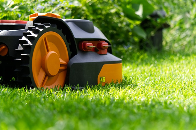 A tight shot of a black and orange robotic lawnmower cutting a lush green lawn.