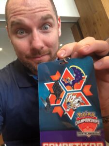 A man holding a competitor badge from a Pokémon tournament. 