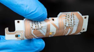Wearable technology - A blue gloved hand holds a flexible printed circuit board with a copper layer on a black background.