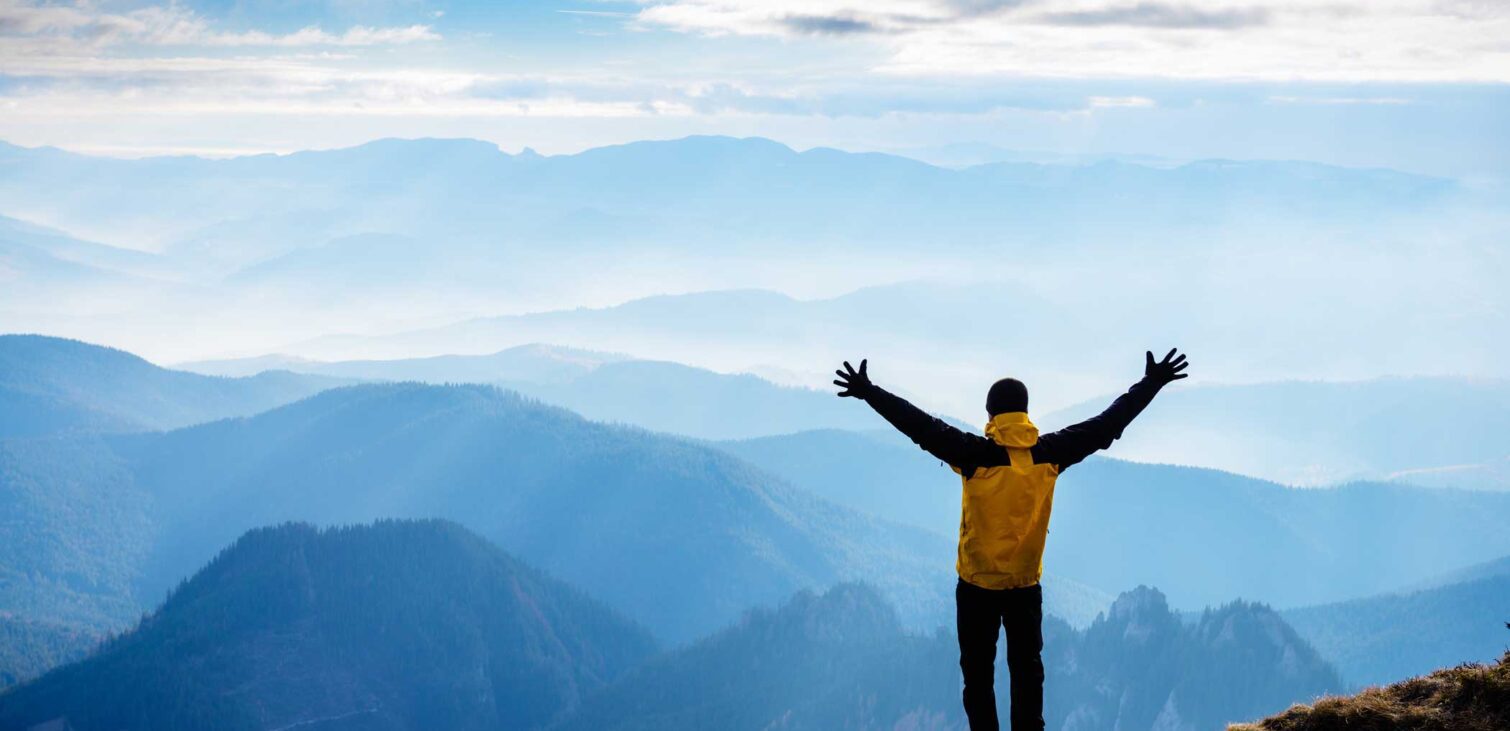 Man stands on mountain with arms raised above head