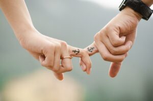 Couple holding hands by their index fingers showcasing matching finger tattoos. 
