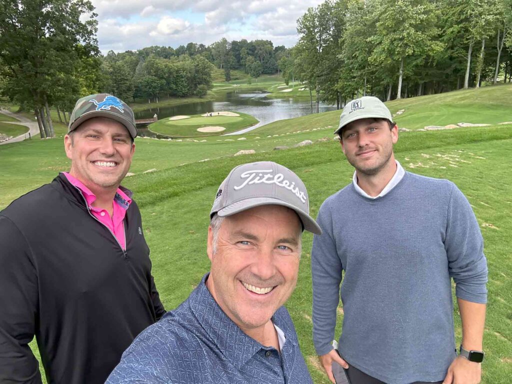 Three men wearing golfing attire smiling and playing golf together. 