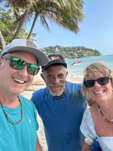 Two men in hats and one woman with sunglasses smiling and enjoying the beach. 