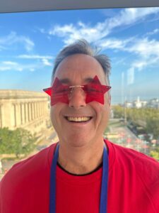 Man smiling in a red shirt with red start sunglasses. 