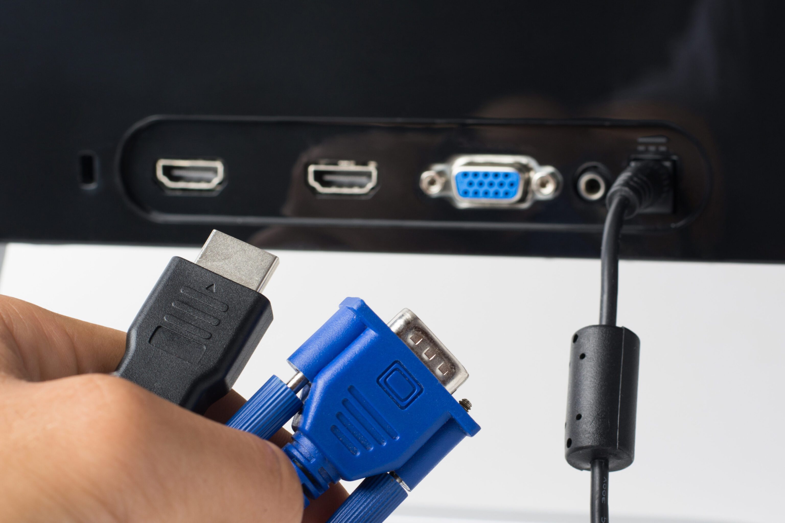 Man’s hand holds HDMI and VGA cables against a monitor with ports