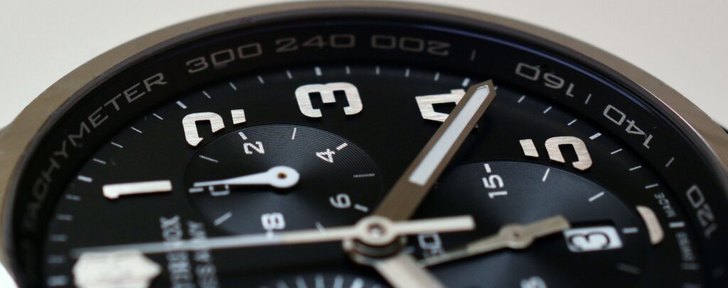 A close-up of a wristwatch with a black dial, bold white numerals, and silver hands.