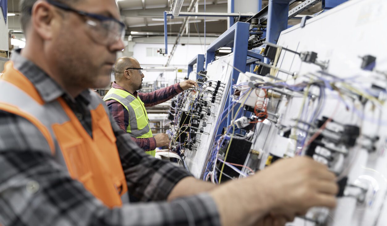 Two manual workers working on the production line in a wire harness assembly factory line.