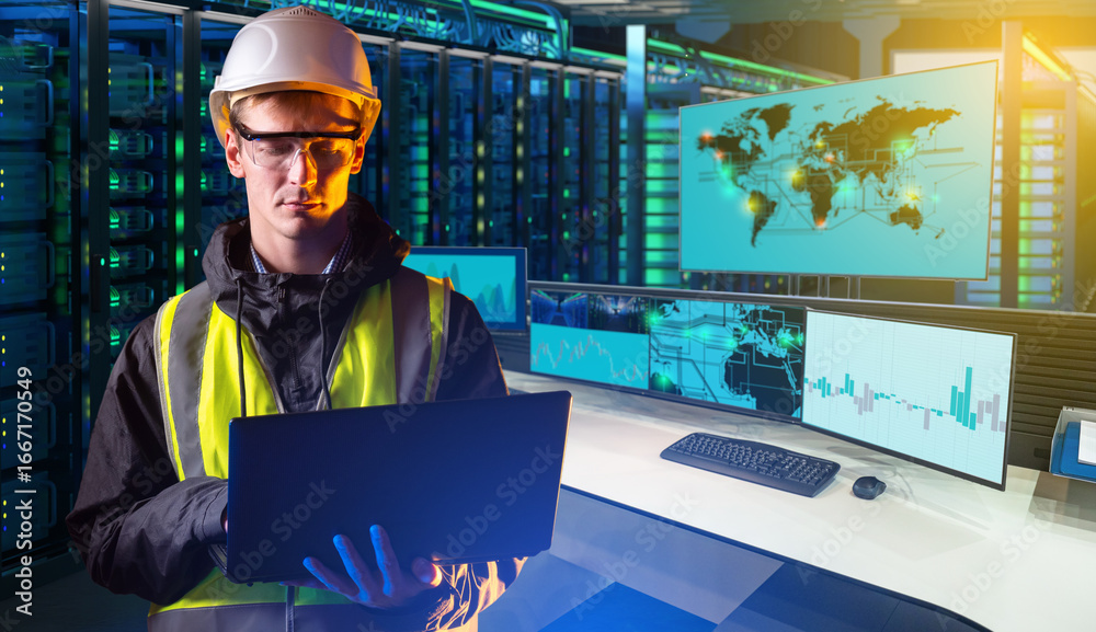 Engineer with a laptop in a data center surrounded by server racks and monitoring screens.
