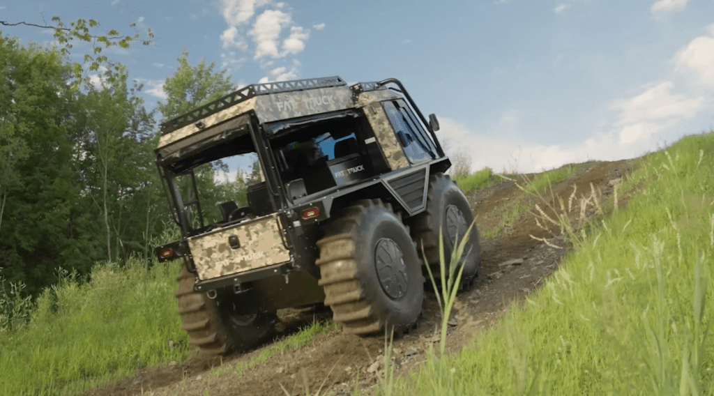 Fat Truck off-road utility vehicle driving up a steep dirt trail in grassy terrain.