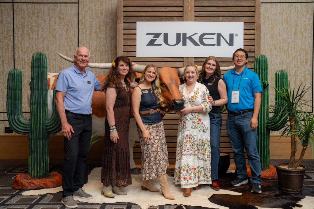 Zuken team members standing in front of a Zuken sign with Texas-themed event decor.
