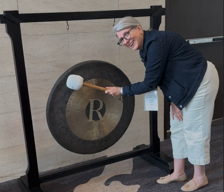 ZIW 2026 attendee smiling while holding a mallet next to a large gong.